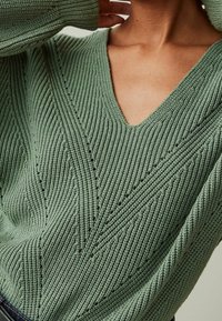 Pull vert en maille avec col en V, texture côtelée et motif diagonal agrémenté de petits détails ajourés sur tout le tissu.