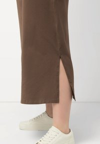 Bruine katoenen rok met zijsplitsen, met een rechte snit en zoom, gecombineerd met witte sneakers voor een casual look.