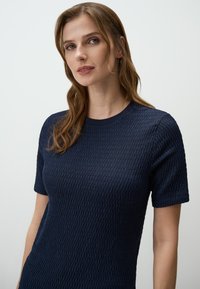 Top corto a maniche corte di colore blu navy con texture, presenta un motivo lavorato a maglia e un collo rotondo. Il tessuto sembra morbido e leggermente in rilievo.
