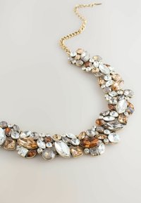 Collana dichiarativa chunky con catena dorata e una varietà di pietre colorate in diverse forme, tra cui goccia e ovale, con accenti scintillanti.