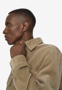 Beige corduroy jacket with a collar and button closure. The texture is ribbed, featuring a front pocket and button cuffs.