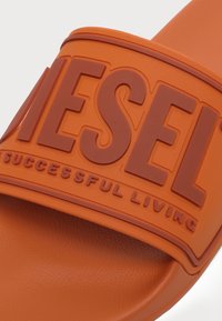 Sandale slide orange avec des lettres en relief orange foncé formant "DIESEL" et un texte plus petit "For Successful Living" sur la bride.