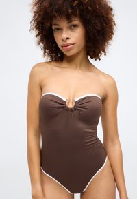 Rudas raukšlėtas liemenėlė be petnešų maudymosi kostiumėlis su baltu apvadu, turintis raktų skylutės detalę centre ir kūną formuojantis siluetas.