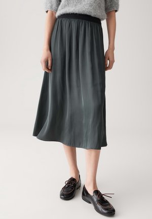 Kobieta ubrana w ciemnoszarą spódnicę midi z elastycznym pasem i czarne sznurowane buty, stoi na jasnym tle.