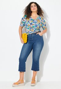 Top con estampado floral y un frente anudado, combinado con unos pantalones capri de mezclilla azul oscuro con encaje. Clutch amarillo brillante y sandalias de plataforma.