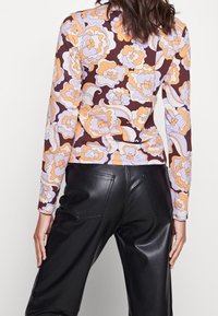 Langärmliges Oberteil im floralen Muster mit Schattierungen von Lavendel, Orange und Braun. Kombiniert mit schwarzen Kunstlederhosen mit Gesäßtaschen.