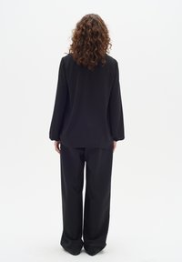 Top nero a maniche lunghe con vestibilità ampia e orlo arrotondato, abbinato a pantaloni neri a gamba larga. Il materiale appare leggero e liscio.