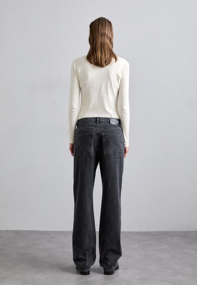 Black denim wide-leg jeans with two back pockets and a high waist, paired with a fitted white long-sleeve top. Minimalist design.