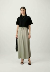 Fekete, rövid ujjas blúz, ami egy hosszú, világosszürke szoknyával van párosítva, amely rugalmas derékkal rendelkezik, fekete szandálokkal és egy fekete táskával kiegészítve.