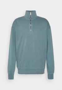 Lichte, teal kleurige pullover sweatshirt met een kwart-rits kraag, ribgebreide manchetten en zoom. Gladde textuur met minimale stiksel details.