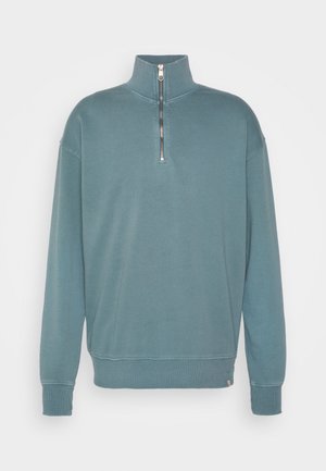 Lichte, teal kleurige pullover sweatshirt met een kwart-rits kraag, ribgebreide manchetten en zoom. Gladde textuur met minimale stiksel details.