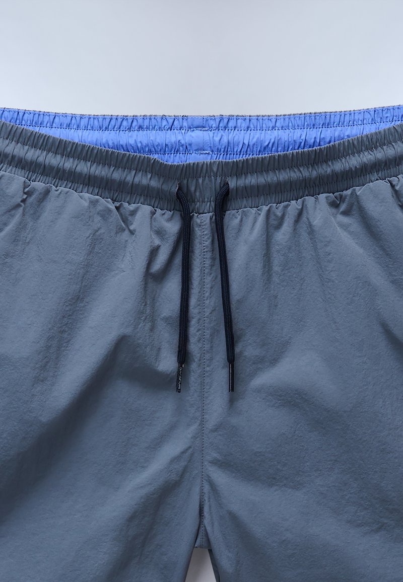 Shorts à taille élastique grise avec une doublure intérieure bleu clair. Dotés d'un cordon de serrage noir, fabriqués dans un matériau léger avec une texture lisse.