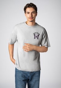 Gray cotton t-shirt with short sleeves, featuring a purple butterfly graphic and "NEW VISION" text printed on the front, worn with blue jeans.
