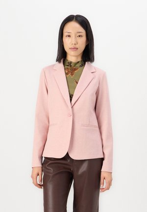 Svetlo roza blazer iz mehkega materiala, ki ima en gumb, izrezane reverje in dva sprednja žepe. Oblečen čez vzorčasto zeleno bluzo.