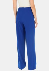 Spodnie o szerokich nogawkach w jasnoniebieskim materiale o gładkiej fakturze. Posiadają wysoki stan i dopasowany krój, z wyraźnym ściegiem z tyłu.