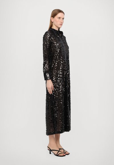 Black sequined dress with a high collar, long sleeves, and a relaxed fit, reaching mid-calf. Paired with strappy black heels.