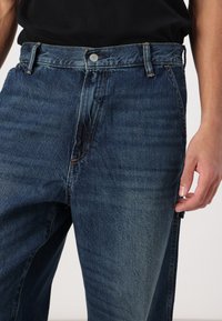 Mørkeblå denim jeans med rette ben, som har en frontknapp, subtile slitasjer og sidelommer. Glatt tekstur.