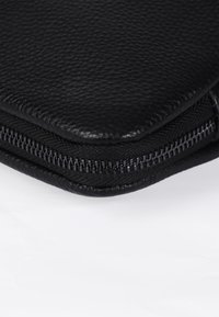 Borsa da viaggio in pelle nera con finitura testurizzata, dotata di una cerniera lucida e dettagli in cucitura lungo i bordi.