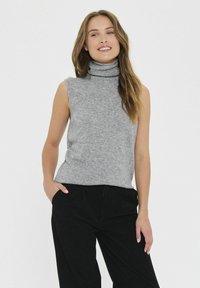 Pulover fără mâneci de culoare gri deschis, dintr-un material tricotat moale. Are un guler înalt și o croială lejeră. Asortat cu pantaloni negri.
