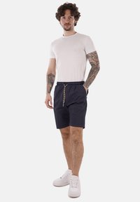 Pantaloni corti blu navy con vita elasticizzata e cordino regolabile, abbinati a una t-shirt bianca aderente e sneakers bianche. Design semplice e casual.