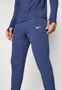 Marineblaue Sporthose mit glatter Textur, schmaler Passform, Reißverschlusstaschen und kleinem weißen Nike-Logo am linken Oberschenkel.