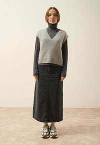 Szary sweter bez rękawów na czarnym golfie, w połączeniu z długą czarną spódnicą dżinsową i sneakersami. Prosty design, miękkie faktury i warstwowy wygląd.