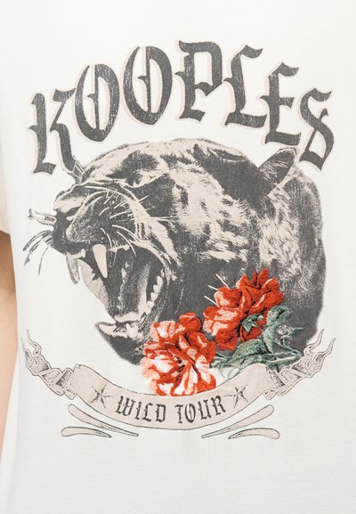 Αρχηγική μαύρη πανθηρα με κόκκινα κεντημένα λουλούδια από κάτω, διακοσμητική κορδέλα με την επιγραφή «Wild Tour» και vintage στυλ κείμενο «Kooples» πάνω από αυτή.