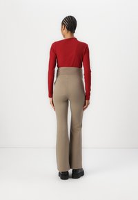 Rood geribbelde lange mouw top gecombineerd met hooggewaisted beige flared broek, gedragen met chunky zwarte laarzen. Minimalistische achtergrond.