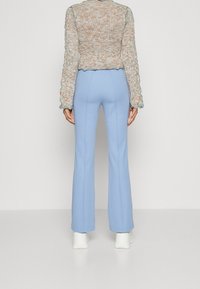 Jasnoniebieskie, rozkloszowane spodnie o gładkiej fakturze, zestawione z krótki, wielokolorowym dzianinowym swetrem z falistymi brzegami.