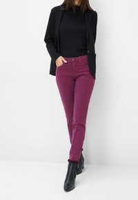 Blazer negro sobre una blusa negra, combinado con pantalones ajustados en color ciruela y botas negras hasta el tobillo. Tejido suave y detalles de diseño a medida.