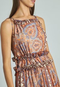 Maxi abito arancione e crema con motivo paisley blu, dotato di orli a balze, spalline regolabili e vita arricciata.