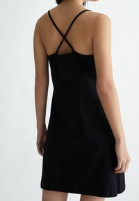 Czarna sukienka bez rękawów o luźnym fasonie, z krzyżującymi się cienkimi ramiączkami i gładką, matową teksturą.