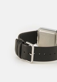 Bracelet de montre en cuir noir avec boucle en métal argenté et boîtier octogonal en argent. Détails notables : bracelet texturé et trous réglables.