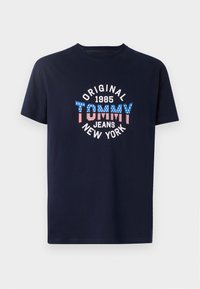 Navy blue cotton t-shirt featuring a circular graphic with "TOMMY" in red and blue with white accents, along with "1985" and "NEW YORK" text.