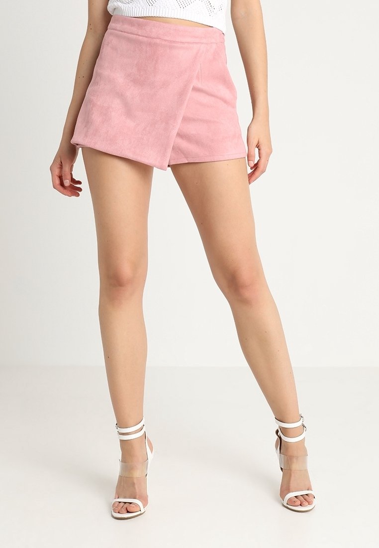 Shorts de ante sintético rosa con una textura suave, cintura alta y abertura lateral. Combinados con tacones blancos con tiras.