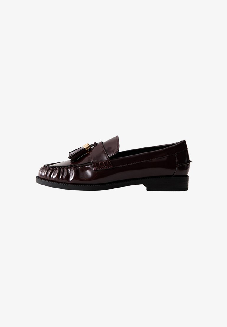 Mocassino in pelle patinata bordeaux con tacco basso, caratterizzato da un design plissettato e dettagli con pon pon sulla vamp. Texture liscia, forma classica.