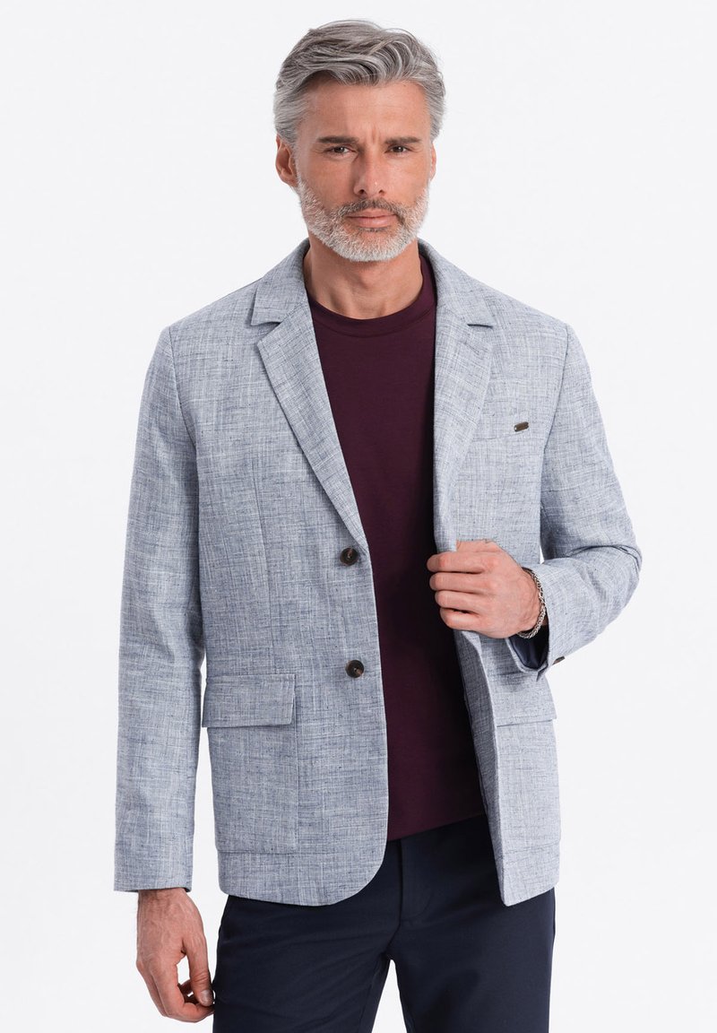 Hellgrauer Leinenblazer mit zwei Knöpfen, Reverskragen und vorderen Taschen, getragen über einem dunkelvioletten T-Shirt.