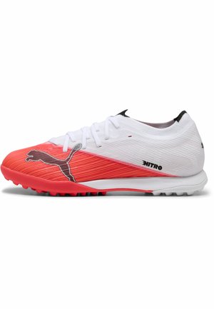 Chaussure de football Puma Nitro blanche et rouge avec lacets, logo Puma noir sur l'avant rouge, et semelle texturée pour surfaces en gazon synthétique.
