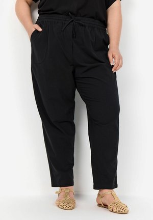 Black elastic-waist trousers with two side pockets, tapered ankle cut, and a textured design. Paired with tan woven flats.