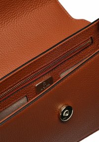 Interno di portafoglio in pelle marrone testurizzata con tasca con cerniera e targhetta metallica del marchio. Bordatura nera distinta intorno all'apertura.