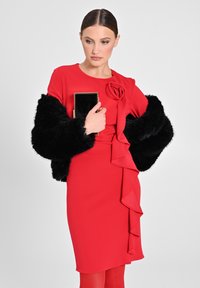 Abito rosso con dettagli arricciati, realizzato in tessuto liscio. Stola in pelliccia sintetica nera sulle maniche. Modello che tiene una piccola pochette con accenti dorati.