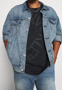 Jasnoniebieska kurtka dżinsowa z kołnierzykiem, dwiema kieszeniami na piersi i srebrnymi guzikami, noszona na ciemnej czarnej koszulce, w połączeniu z dżinsami.