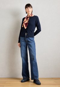 Navy cardigan with round neckline, button detailing, and a smooth texture, paired with flared denim jeans and a patterned silk scarf.