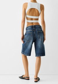 Top corto bianco a coste con schiena scoperta e cinturini laterali, abbinato a pantaloni bermuda in denim blu con vestibilità comoda e tasche posteriori.