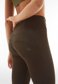 Leggings marroni a vita alta con dettagli di cucitura curvi e un logo sulla tasca posteriore, realizzati in un tessuto elastico e liscio.