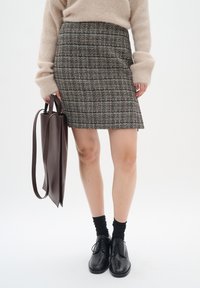 Tume toonides ruuduline tweed mini-seelik, mis on sobitatud mustade pitsidega kingade ja pruuni nahast käekotiga. Pehme beeži värvi sviiter.