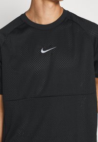 Svart tränings t-shirt tillverkad av andningsbart mesh-material. Har korta ärmar, rund halsringning och reflekterande Nike-logga p å bröstet.