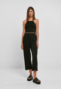 Crni rebrasti crop top u kombinaciji s crnim, širokim hlačama do sredine tele. Model nosi sandale s platformom. Jednostavan i skladan dizajn.