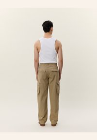 Khaki cargo kalhoty se bočními a zadními kapsami, kombinované s bílým tílkem. Celkový design je volný s rovnými nohavicemi.