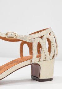 Béžové sandály na blokovém podpatku, s texturovaným textilním svrškem a výřezovými detaily. Stélky mají hnědou polstrovanou plochu pro pohodlí.